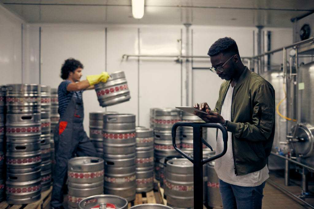  Two beer distributors stack kegs onto skids while tracking stock on a tablet