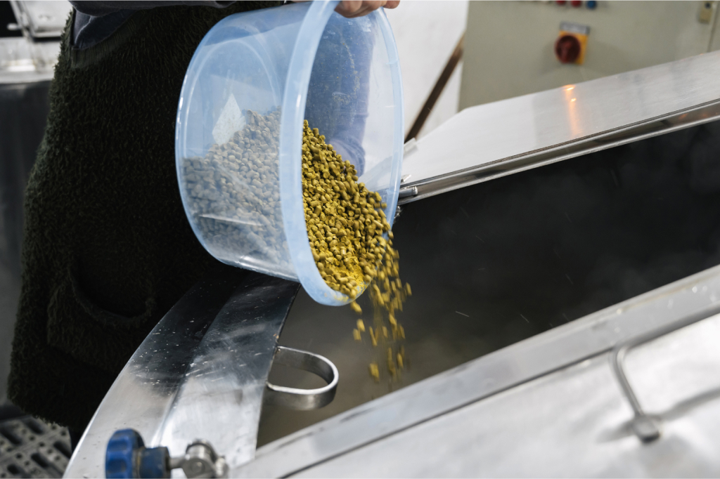 A brewer pours hops into a fermentation tank
