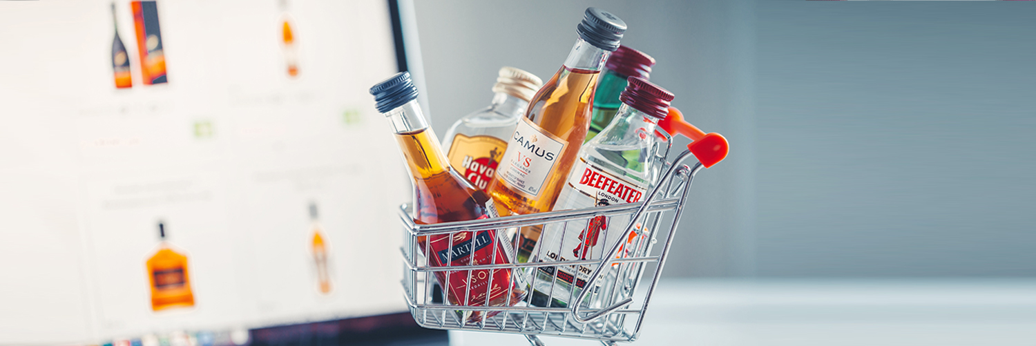 A miniature shopping cart filled with liquor bottles is seen on a laptop