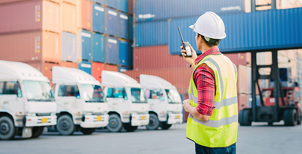 Logistics personnel using a walkie-talkie to coordinate logistical issues at a shipping yard