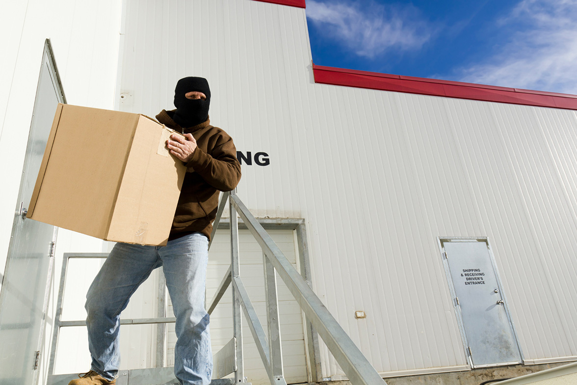 Thief in a balaclava leaving a warehouse with a box