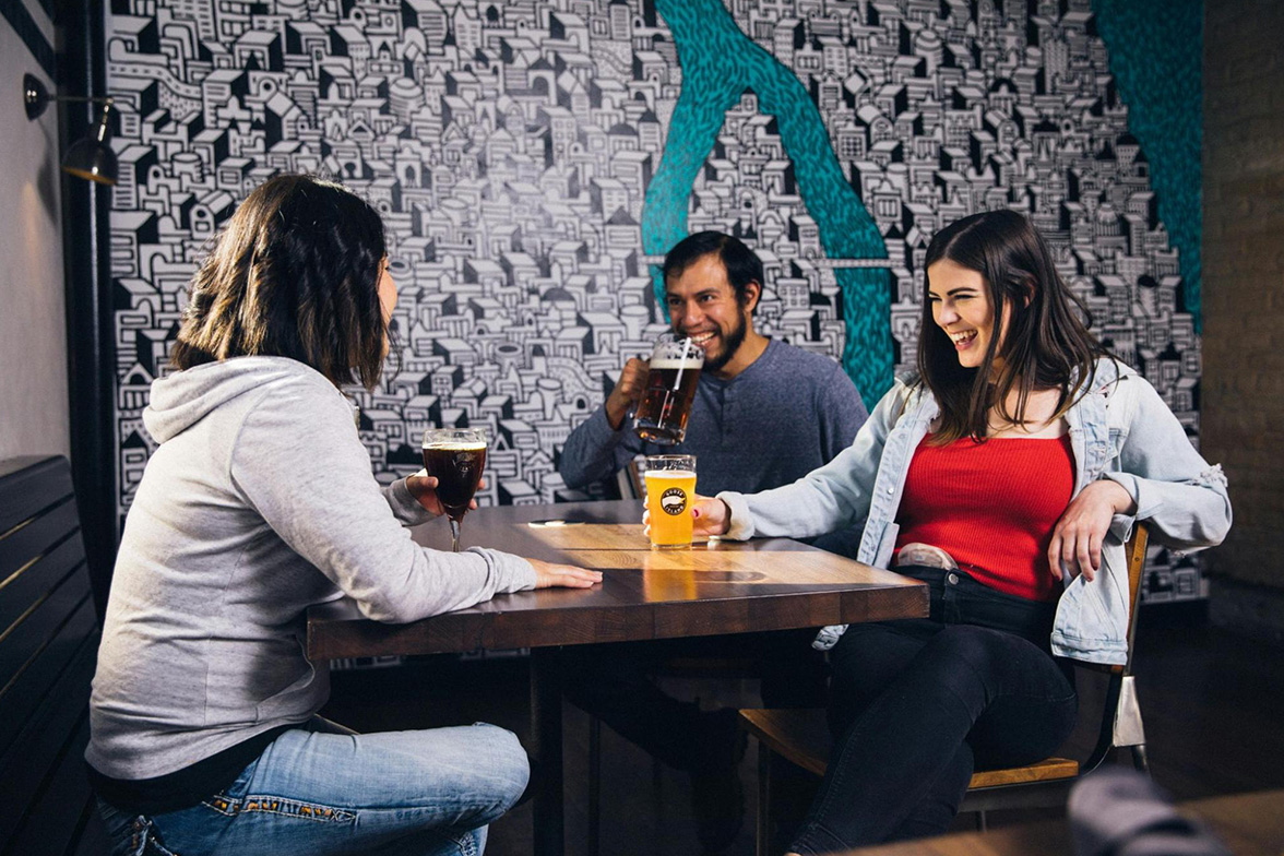 Three friends hanging out in a pub drinking beer, laughing