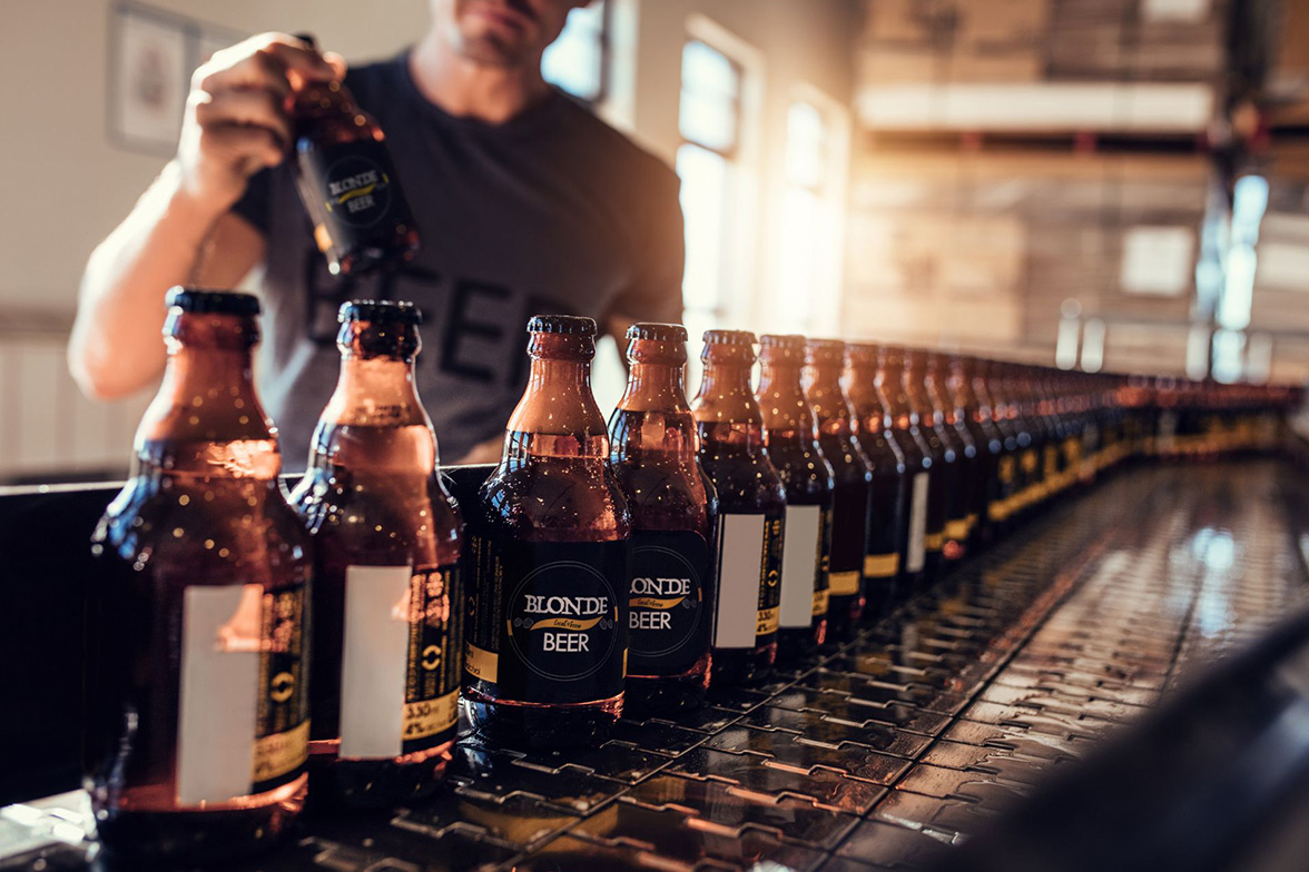 A conveyor belt of beer bottles with a beverage startup owner conducting quality control
