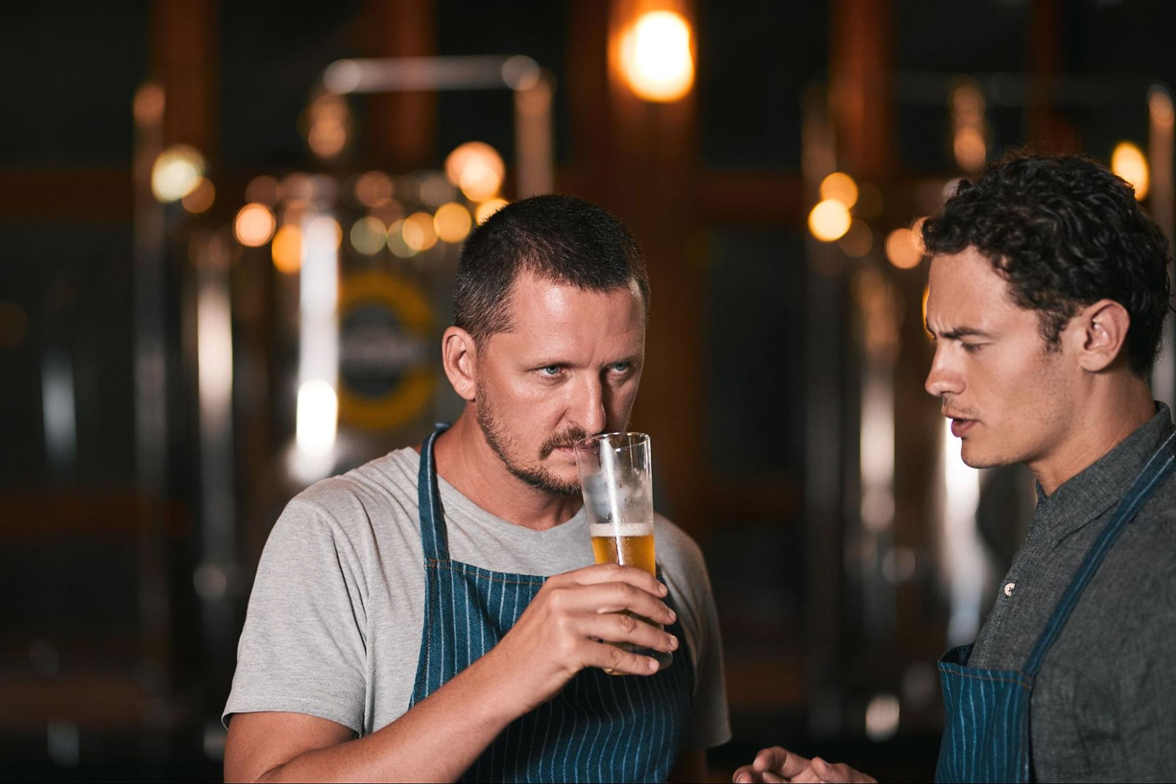 Two brewers smelling and taste-testing a glass of beer