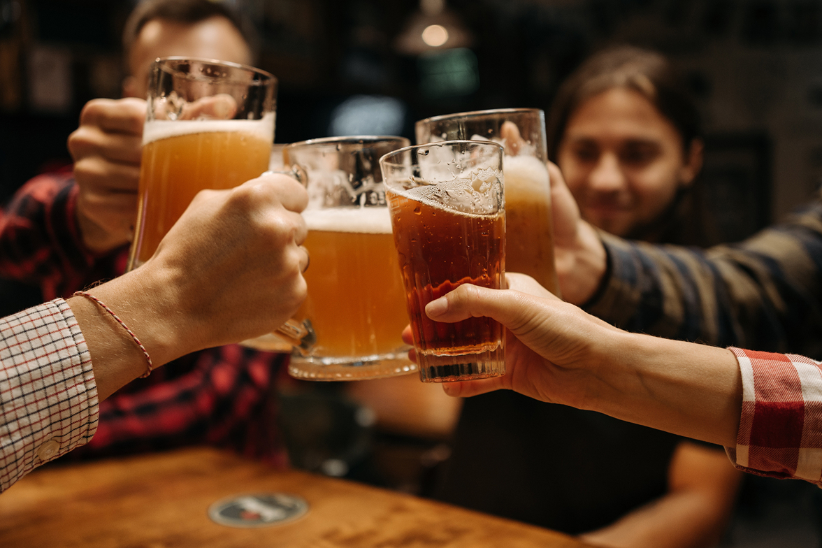 Four people clink/cheer their pints of beer together at a table.