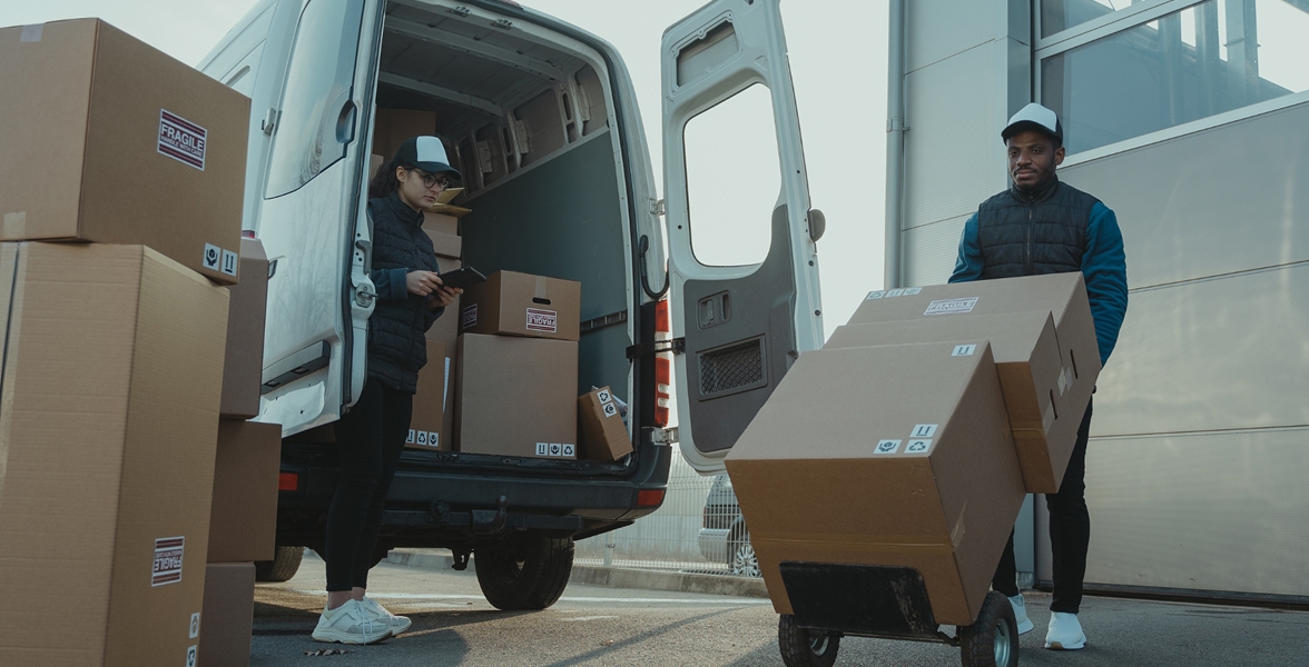 A pair of employees move boxes around a delivery van.