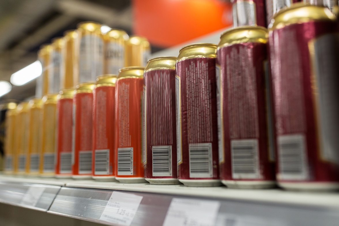 Beverage cans, with labels varying in color, are displayed on a shelf in a store. 