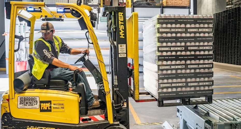 A person using a forklift moves skids of craft beer.
