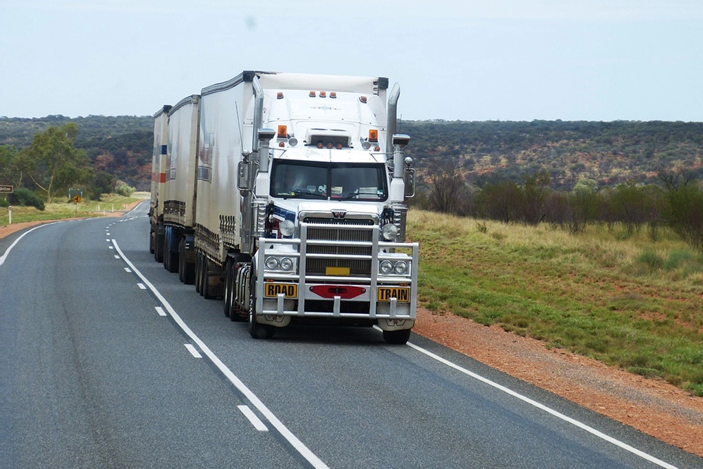 A freight truck drives along a two-lane highway through forested plains