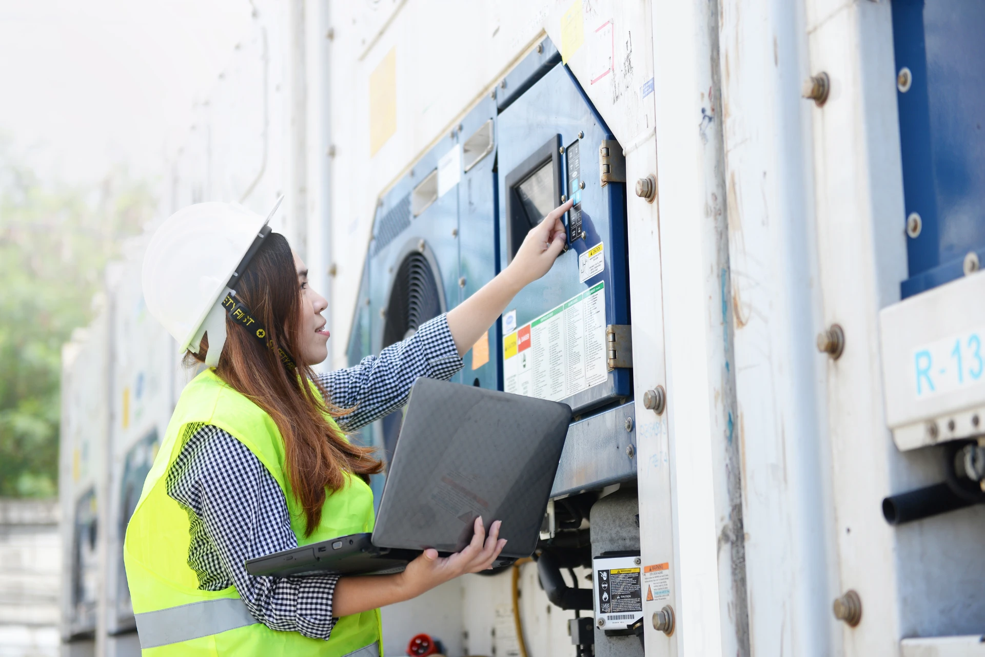 Technician wearing a hard hat and safety gear checking the temperature of a reefer container