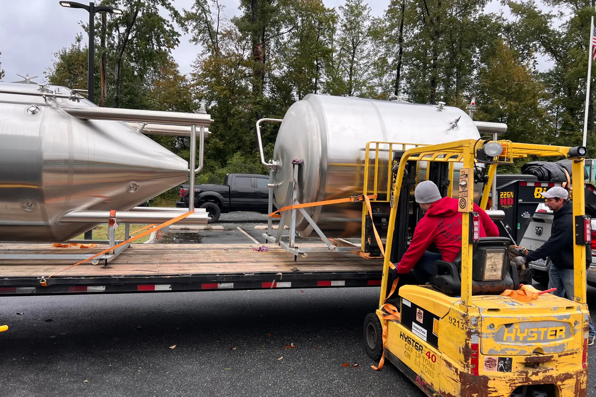 Logistics professionals using a forklift to move brewing equipment from a flatbed
