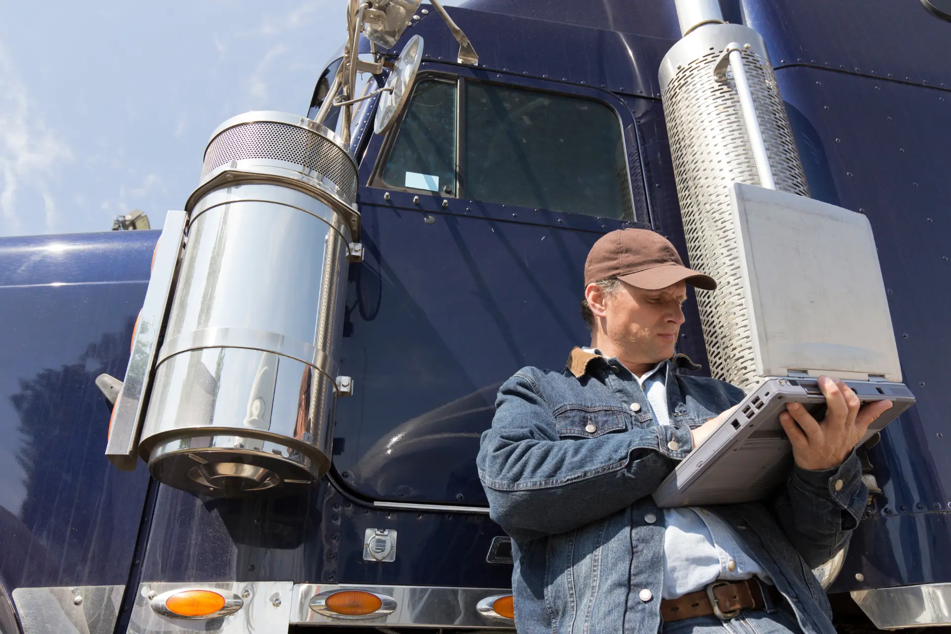 A trucker using a laptop while leaning on a blue truck 