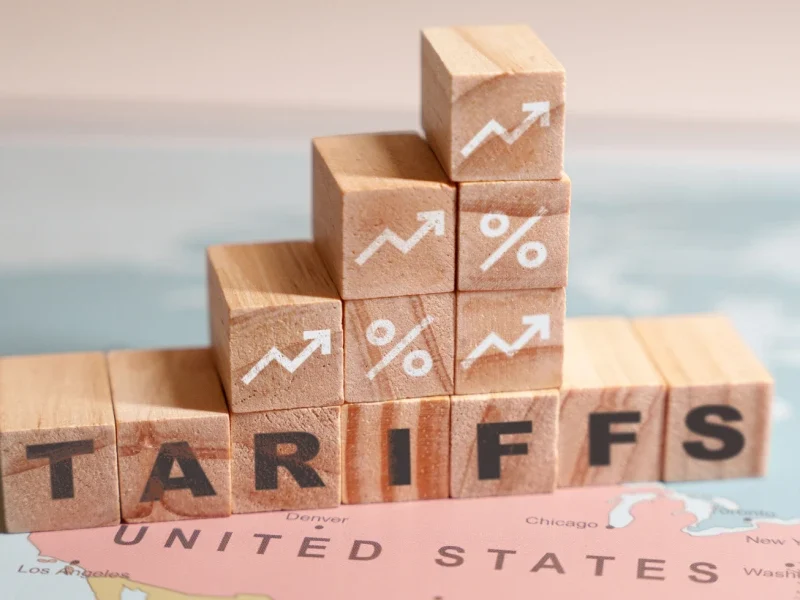 Wooden blocks spelling TARIFFS are placed on a map of North America, specifically over the United States