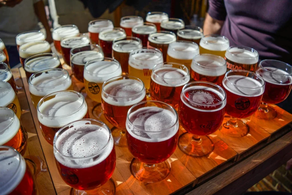 A wooden tray filled with numerous small glasses of beer in various shades