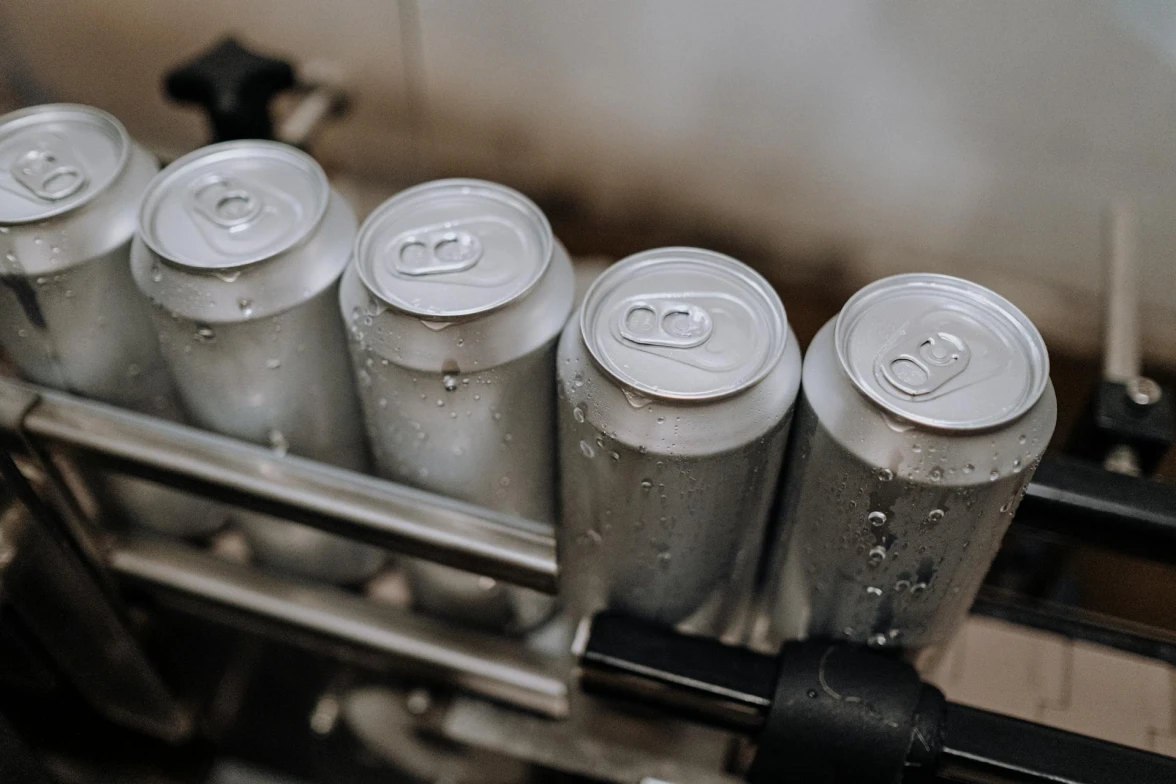 A row of unlabeled aluminum cans with condensation moves along a conveyor system