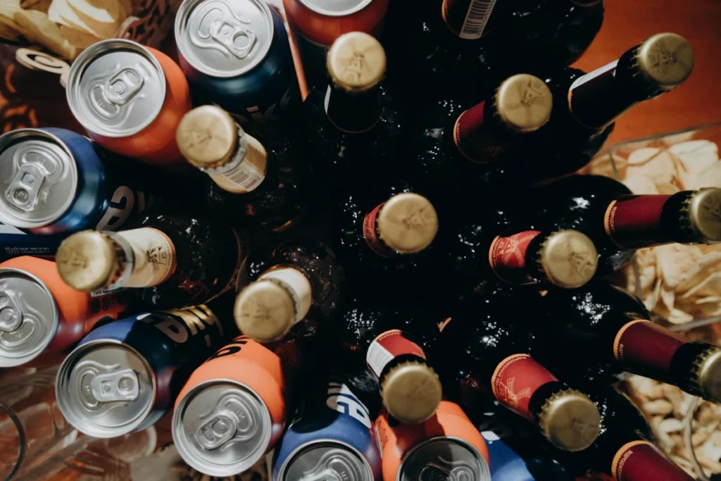 Top view of assorted beer bottles and cans arranged in a group with snacks nearby.
