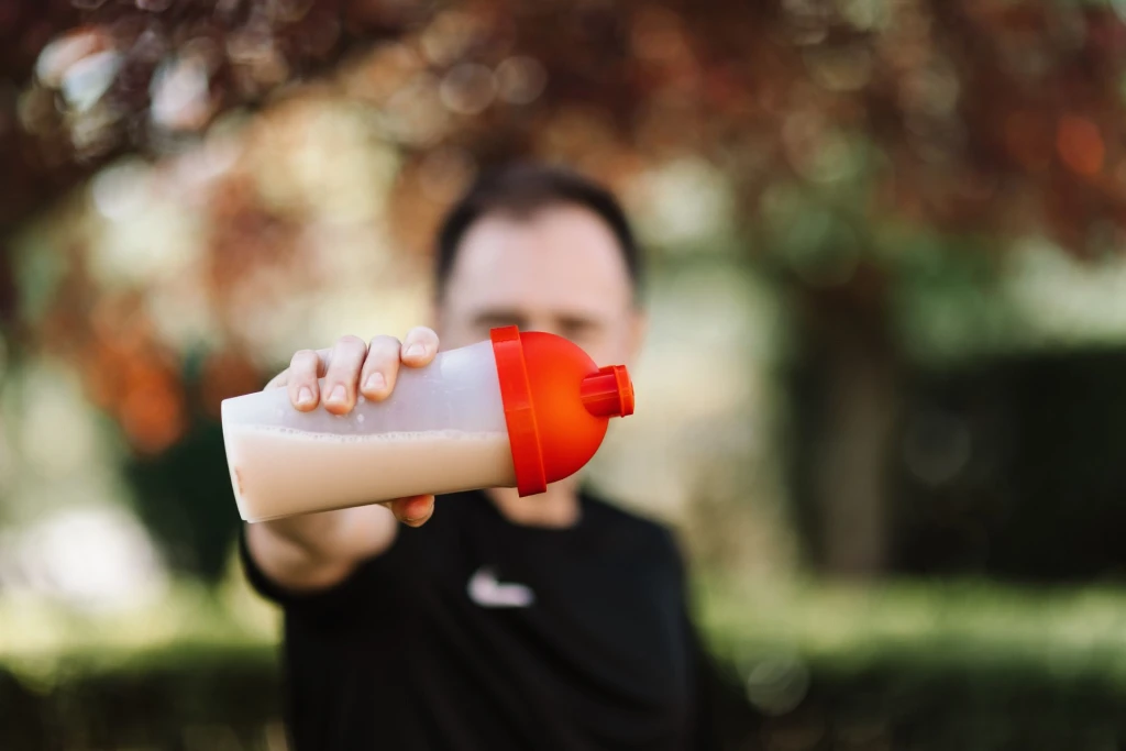 A man holding a plastic protein shake tumbler outdoors with a blurred background