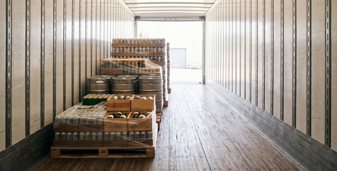 A partially loaded semi-truck trailer with pallets of cans and kegs, showing empty space in the rear